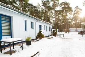 A white building with blue accents, a bench, a potted plant, and a snow-covered ground.