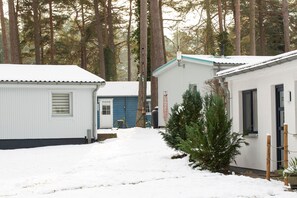 Une rangée de cabanes, la terre étant recouverte de neige, le tout entouré de grands arbres.