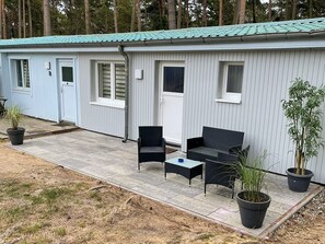Een gelijkvloerse stacaravan met een overdekte patio, twee stoelen, een kleine tafel en potplanten.