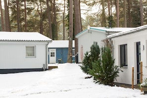 Een rij blokhutten met een besneeuwde ondergrond, omgeven door hoge bomen.