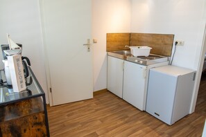 Een compacte keuken met een koelkast, fornuis en een koffieapparaat op een glazen tafel.
