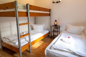 Een slaapkamer met een stapelbed, een houten ladder, een klein tafeltje met een lantaarn en een keurig opgemaakt bed.