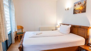 A single bed with a wooden headboard, a bedside table with a lamp, a chair, and a window with curtains. - Vacation apartment 15 - Ferienanlage Zum Knirk (Lubmin (Seebad))