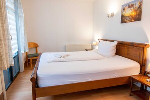Een enkel bed met een houten hoofdbord, een nachtkastje met een lamp, een stoel en een raam met gordijnen.