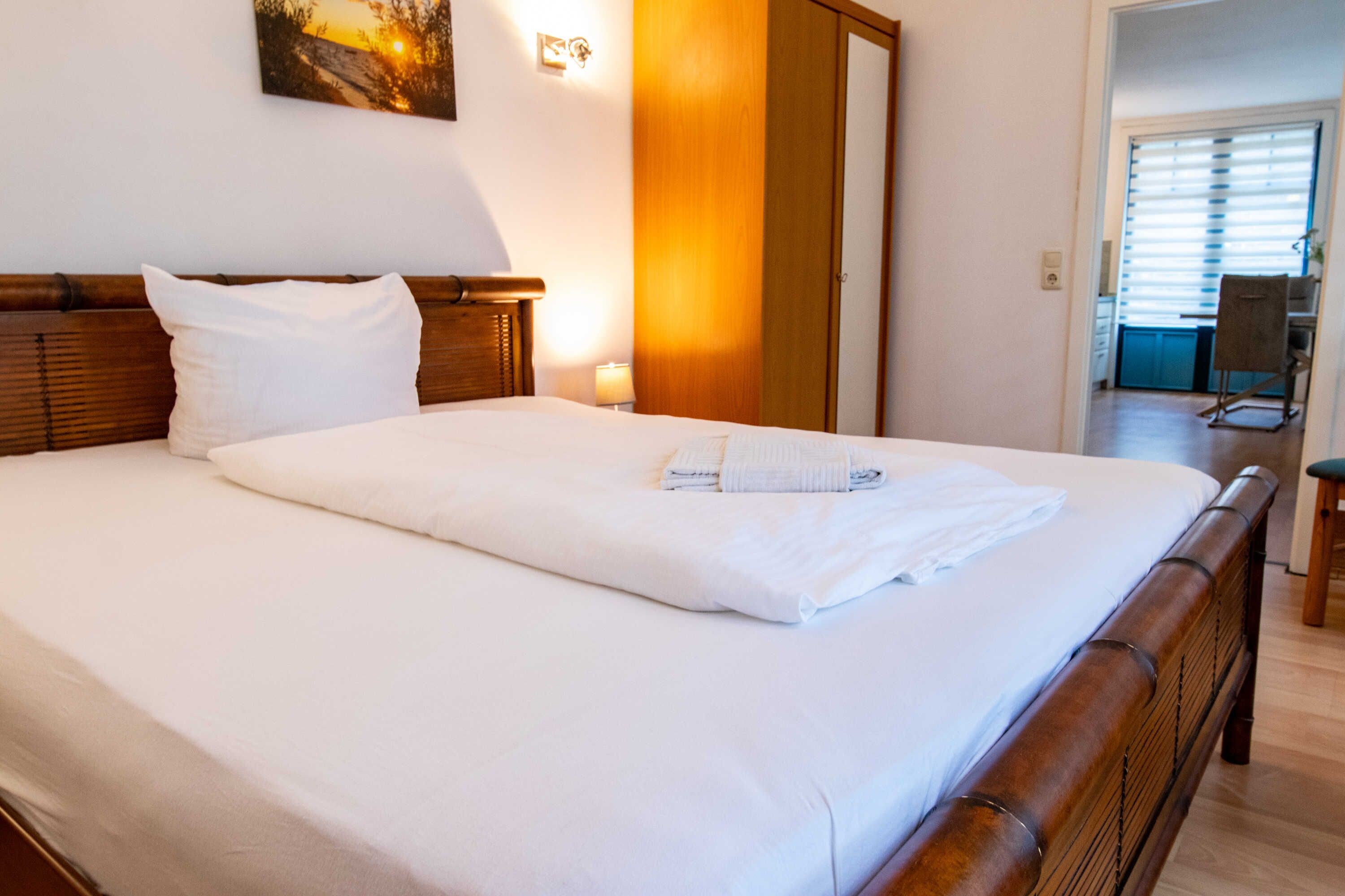 A neatly made bed with white linens, a wooden headboard, and a wall-mounted picture.