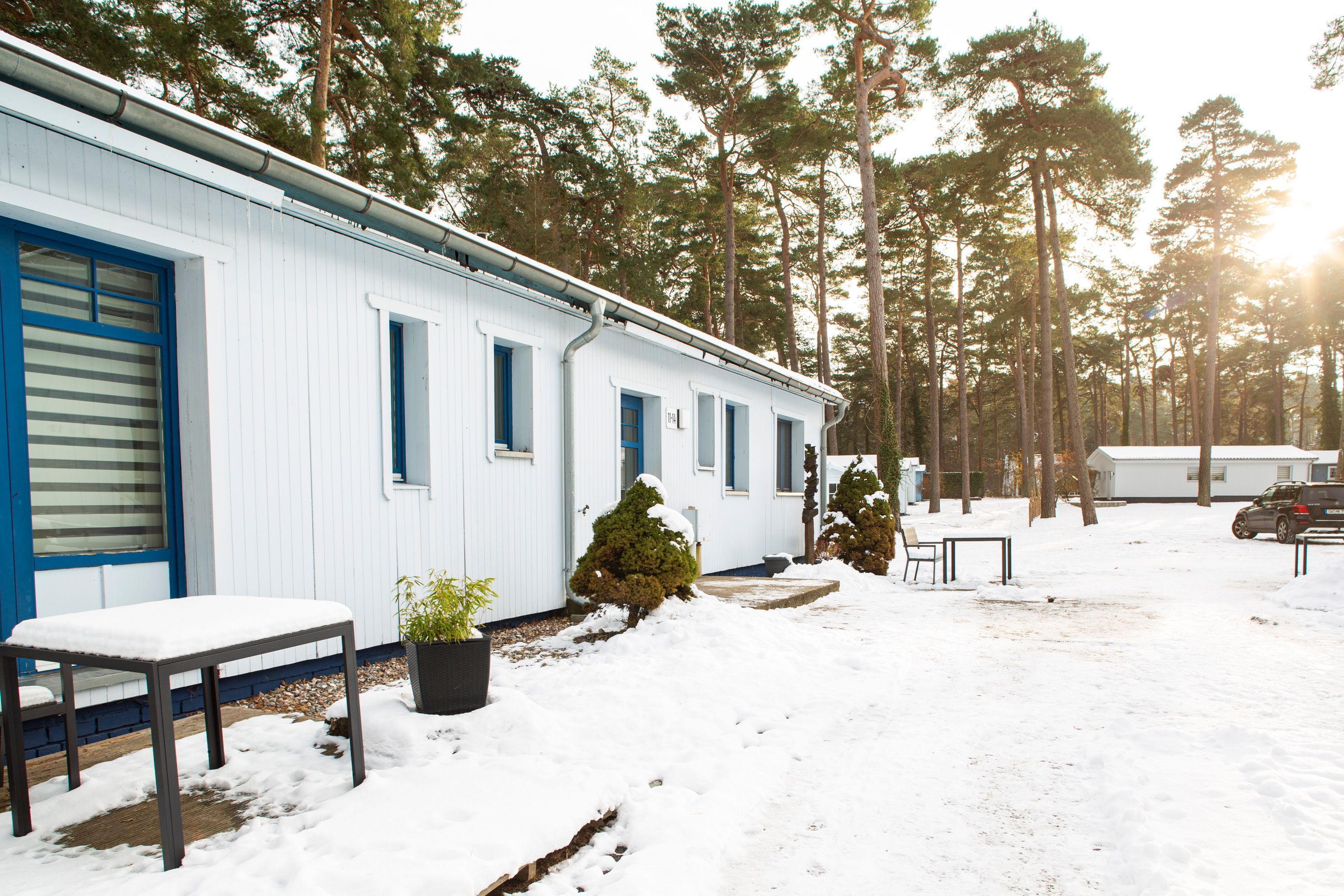 A white building with blue accents, a bench, a potted plant, and a snow-covered ground.