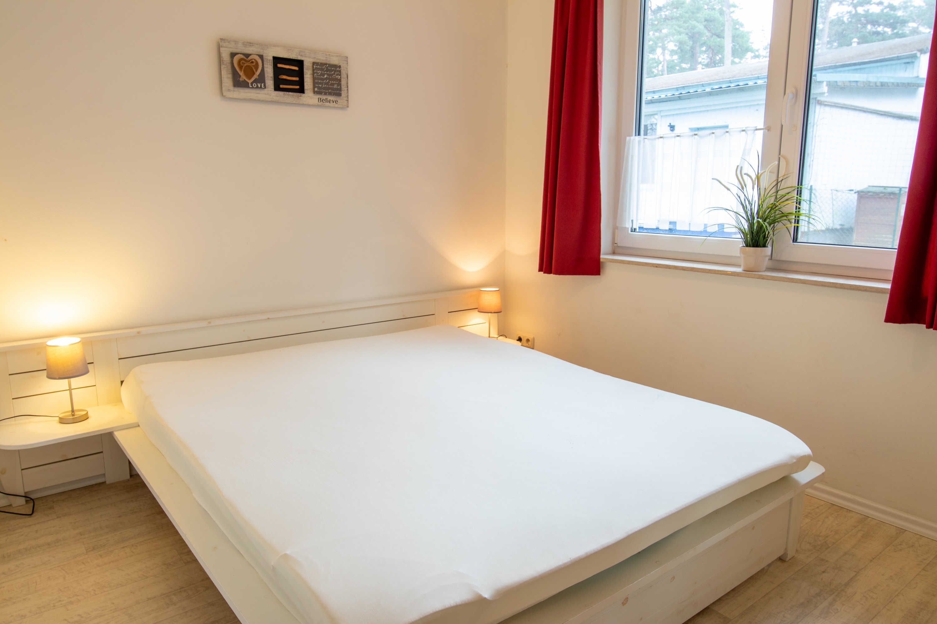 A bedroom with a bed, bedside lamps, a window with a view, and a wall-mounted plaque.