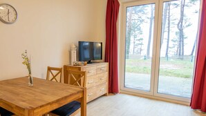 Quarto com uma mesa de jantar de madeira, uma TV sobre um armário de madeira e uma grande porta de vidro deslizante que dá para uma área externa.