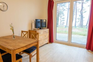 Ein Zimmer mit einem Holzesstisch, einem Fernseher auf einer Holzkommode und einer großen Schiebeglasdoor zur Außenfläche.