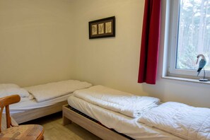 Una habitación con dos camas individuales, una silla de madera, un cuadro en la pared y una ventana con vistas a árboles.