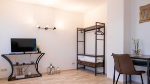 A room with a bunk bed, a desk, a chair, a TV, and wall-mounted lights. - Apartment 21 - Resort Zum Knirk (Lubmin (Seebad))