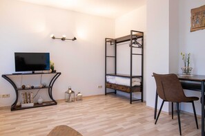 Een kamer met een stapelbed, een bureau, een stoel, een televisie en wandlampen.