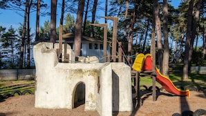 A playground with a slide and climbing structures, surrounded by trees. - Apartment 21 - Resort Zum Knirk (Lubmin (Seebad))