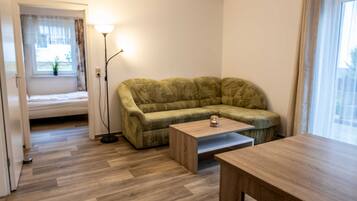 Ein Zimmer mit einem grünen Sofa, einem Holztisch, einer Lampe und einem Fenster mit Vorhängen.
