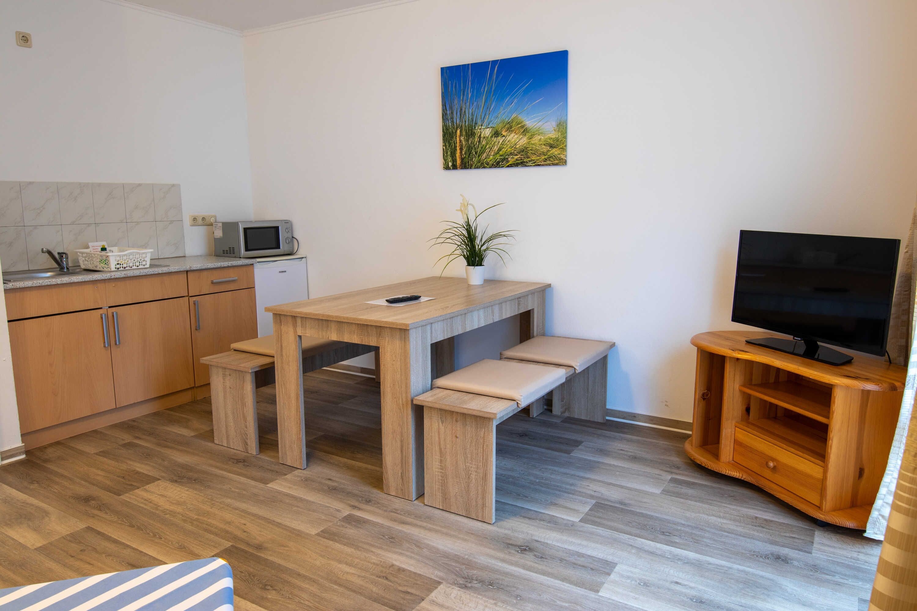 Een moderne keuken met een magnetron, houten kastjes, een eettafel met banken, een kamerplant en een tv op een houten dressoir.