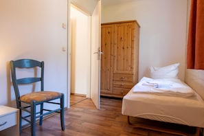 A bedroom with a wooden wardrobe, a single bed, a chair, and a desk.