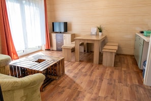 A room with a wooden floor, a television on a cabinet, a table, and a chair.
