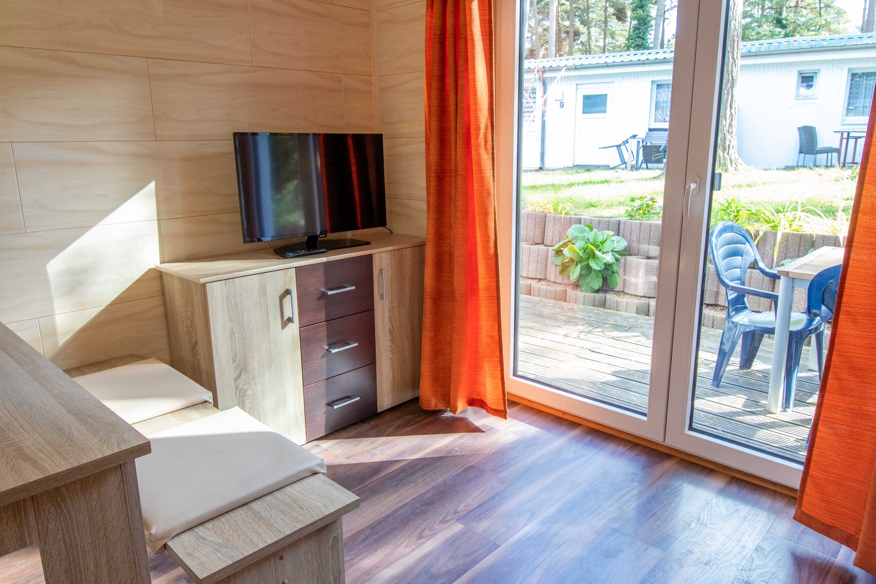 A room with a wooden cabinet, a television, and a sliding glass door leading to an outdoor area with chairs and a table.