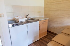 Een kleine keuken met een geïntegreerde koelkast, een spoelbak en houten keukenkastjes.