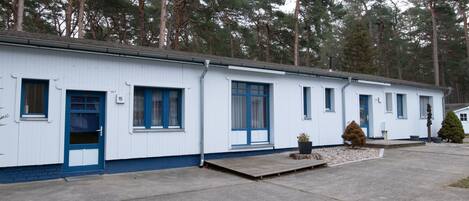 A row of white mobile homes with blue trim, numbered doors, and a small front porch area.