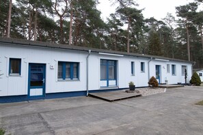 Een rij witte stacaravans met blauwe accenten, genummerde deuren en een klein voortuintje.