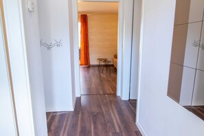 Un pasillo con piso de madera, una pequeña mesa y una silla al fondo.