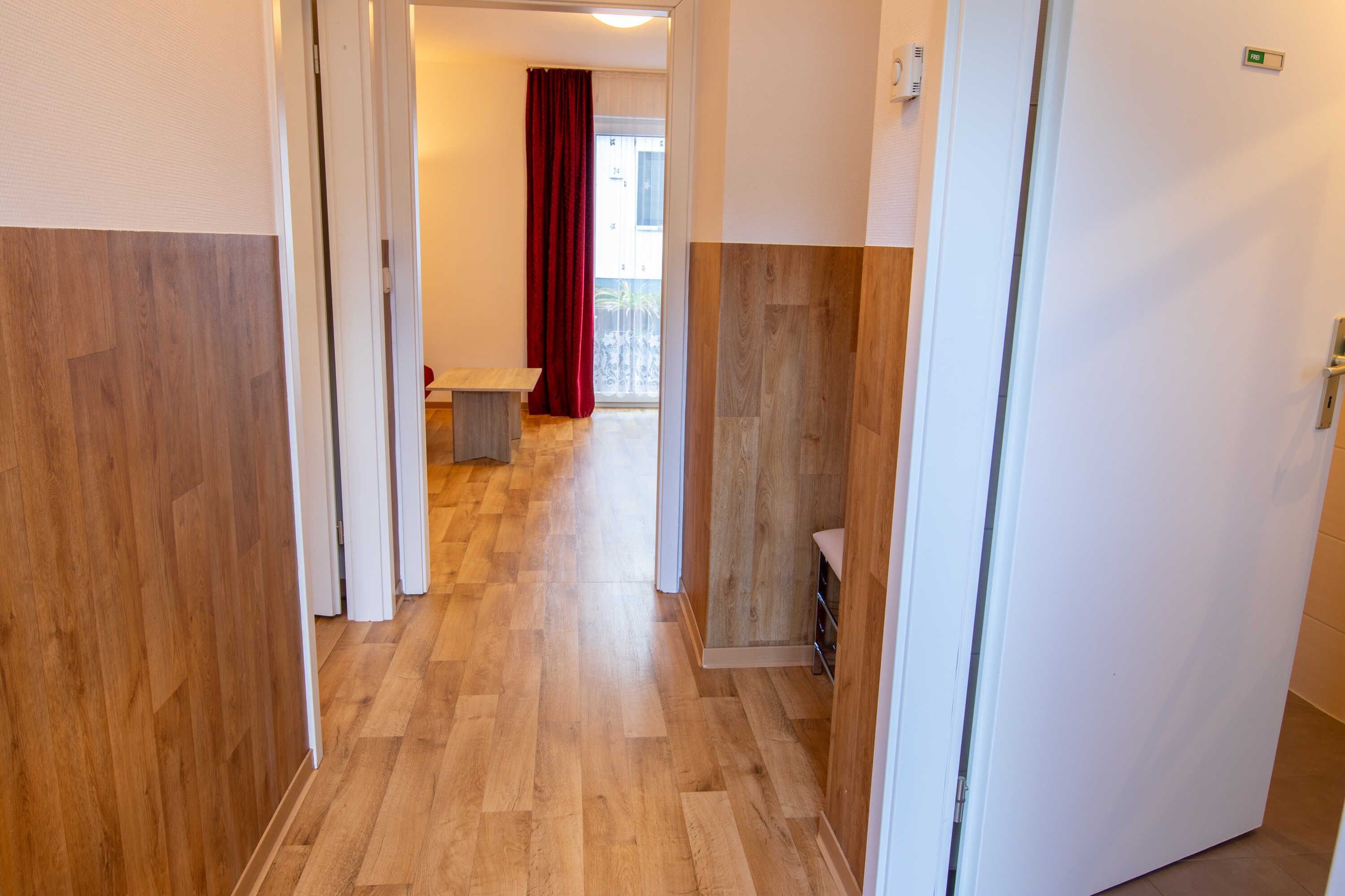 A hallway with wooden flooring, a door on the right, and a view into a room with a red curtain.