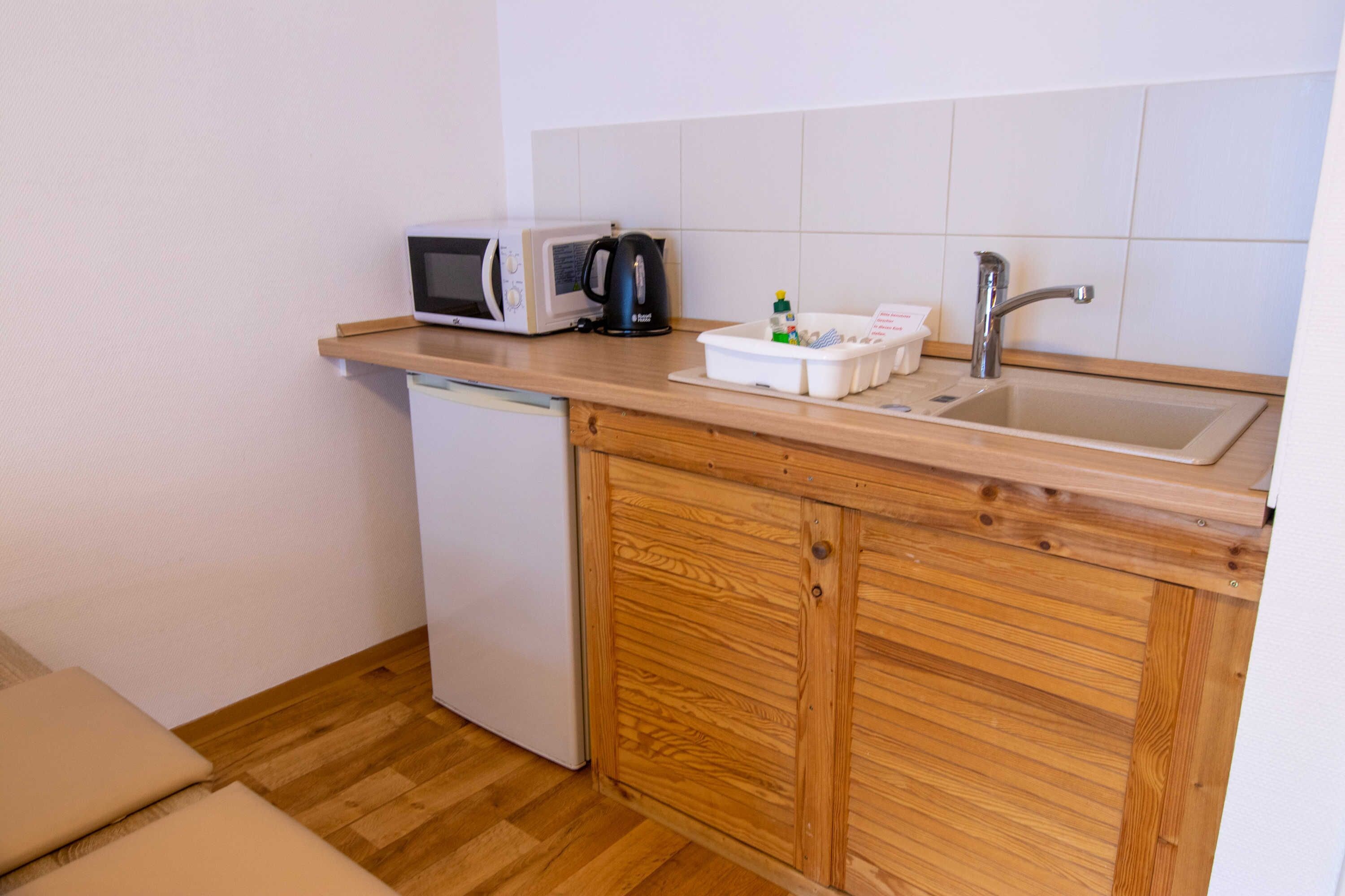 Een kleine keuken met een magnetron, waterkoker en spoelbak.