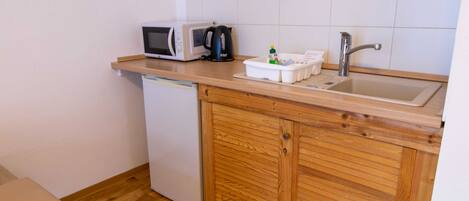 A compact kitchenette with a microwave, kettle, and sink.