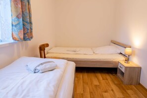 Een kleine, schone kamer met twee enkele bedden, een houten nachtkastje met een lamp en een raam met gordijnen.