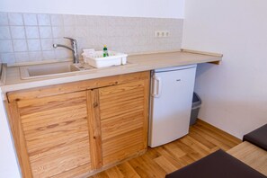 Eine kleine Küchenzeile mit Spüle, kleinem Kühlschrank und Mülleimer.