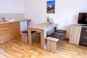 Eine moderne Küche mit Holzschränken, einem eingebauten Geschirrspüler, einem Holzessttisch mit Bänken und einem Flachbildfernseher auf einem Schrank.