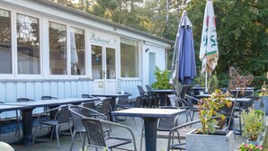 En restaurant med udendørs siddepladser, herunder borde og stole, samt et overdækket område med parasoller.