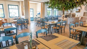 Un comedor amplio con múltiples mesas y sillas, una isla central con electrodomésticos de cocina, y ventanas grandes que dejan entrar luz natural.