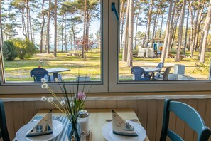 A dining table with chairs, a vase with flowers, and a view of a park with trees and a playground. - Vacation apartment 8 - Ferienanlage Zum Knirk (Lubmin (Seebad))