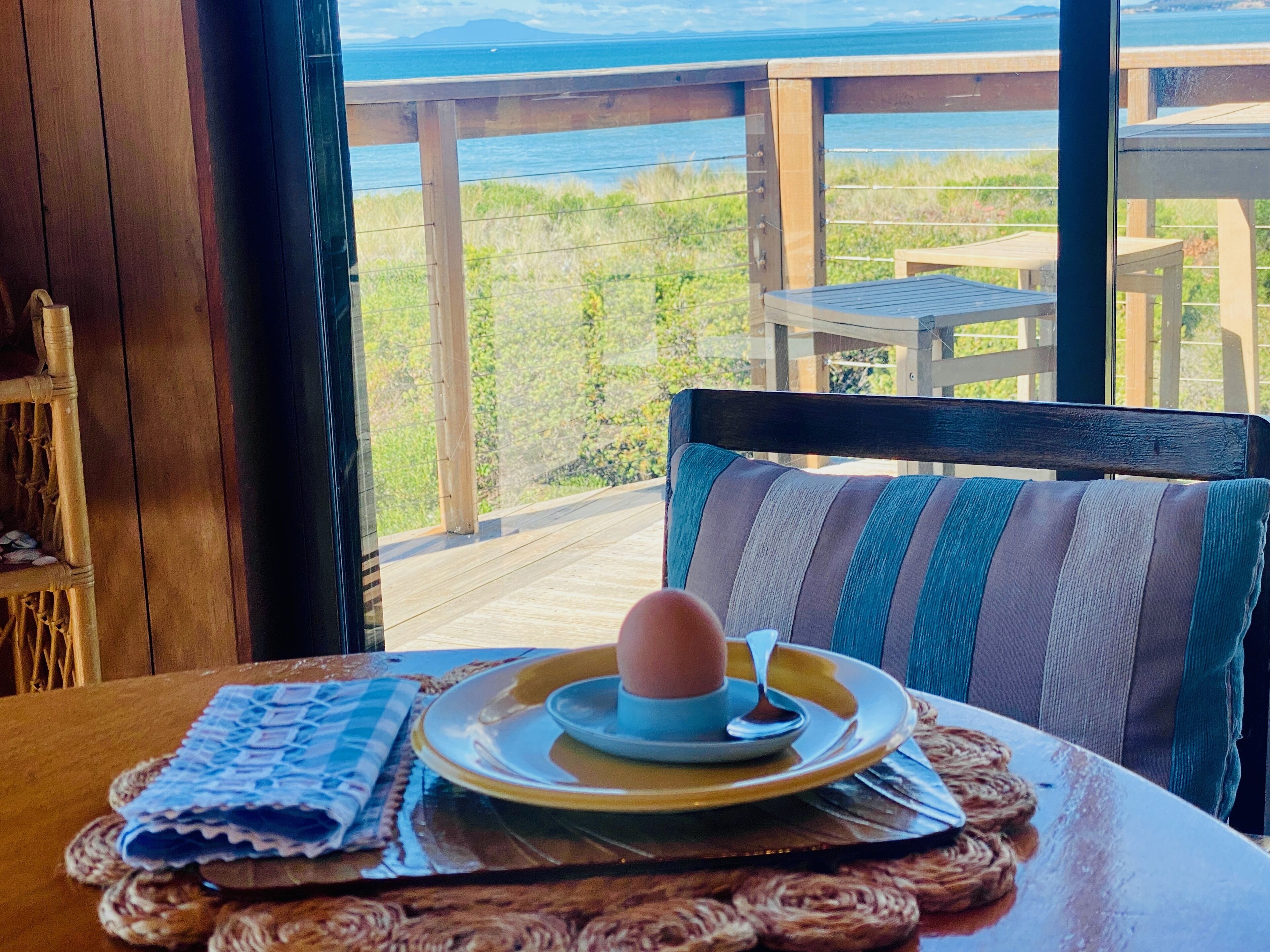 Une table à manger avec une assiette de nourriture, une chaise et une vue sur l’océan.