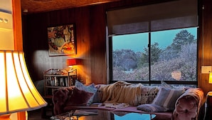A cozy living room with a large window, a sofa, a glass coffee table, and a red chair. - Mid-century beach front house, on five private acres, dogs welcome (Dolphin Sands)