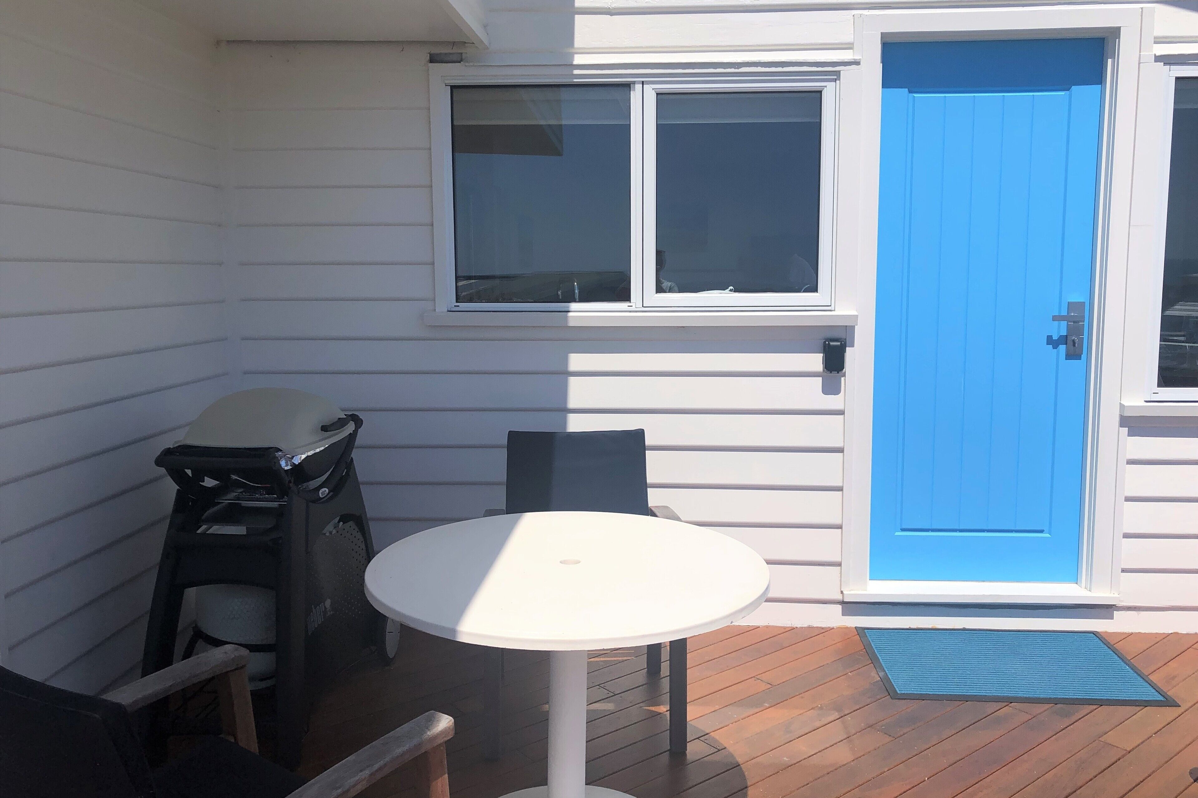 A patio with a white table and chairs, a blue door, and a window with blinds.