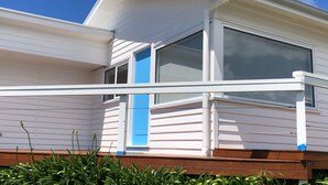 En vit husvagn med en blå dörr, stora fönster och en träveranda.