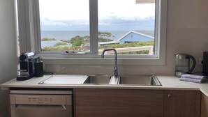 Ett kök med en diskho i rostfritt stål, en kaffebryggare och utsikt över havet genom ett fönster.