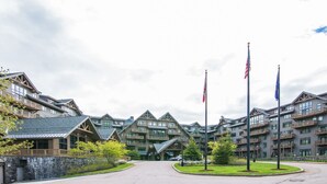 A multi-story hotel with a stone facade, balconies, and a central entrance. - Lodge at Spruce Peak! Amazing 2 BR ! Ski In-Out! (Stowe)