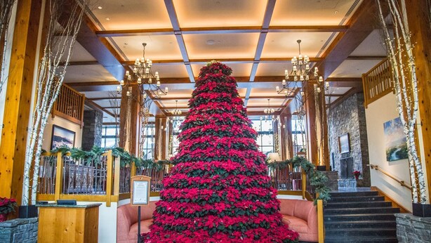 A grand lobby with a large Christmas tree, wooden paneling, and a staircase. - Lodge at Spruce Peak! Amazing 2 BR ! Ski In-Out! (Stowe)