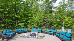 An outdoor seating area with wicker furniture and blue cushions, surrounded by a stone fire pit and a metal fence. - Lodge at Spruce Peak! Amazing 2 BR ! Ski In-Out! (Stowe)