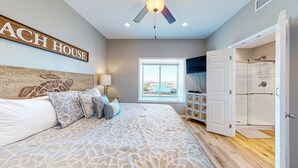 A bedroom with a bed, a ceiling fan, a window, and a door leading to a bathroom.