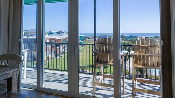 A balcony with a view of the ocean, a wooden chair, and a table.