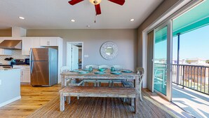 A spacious dining area with a wooden table and chairs, a modern kitchen with stainless steel appliances, and a large window offering a view of the neighborhood.