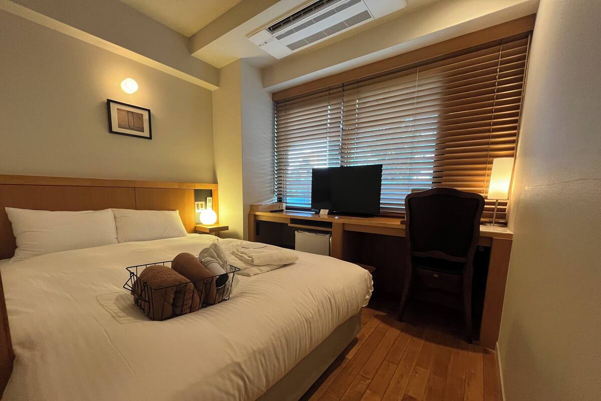 Ein Hotelzimmer mit Bett, Schreibtisch mit Computer, Stuhl, Fernseher und Nachttischlampe.