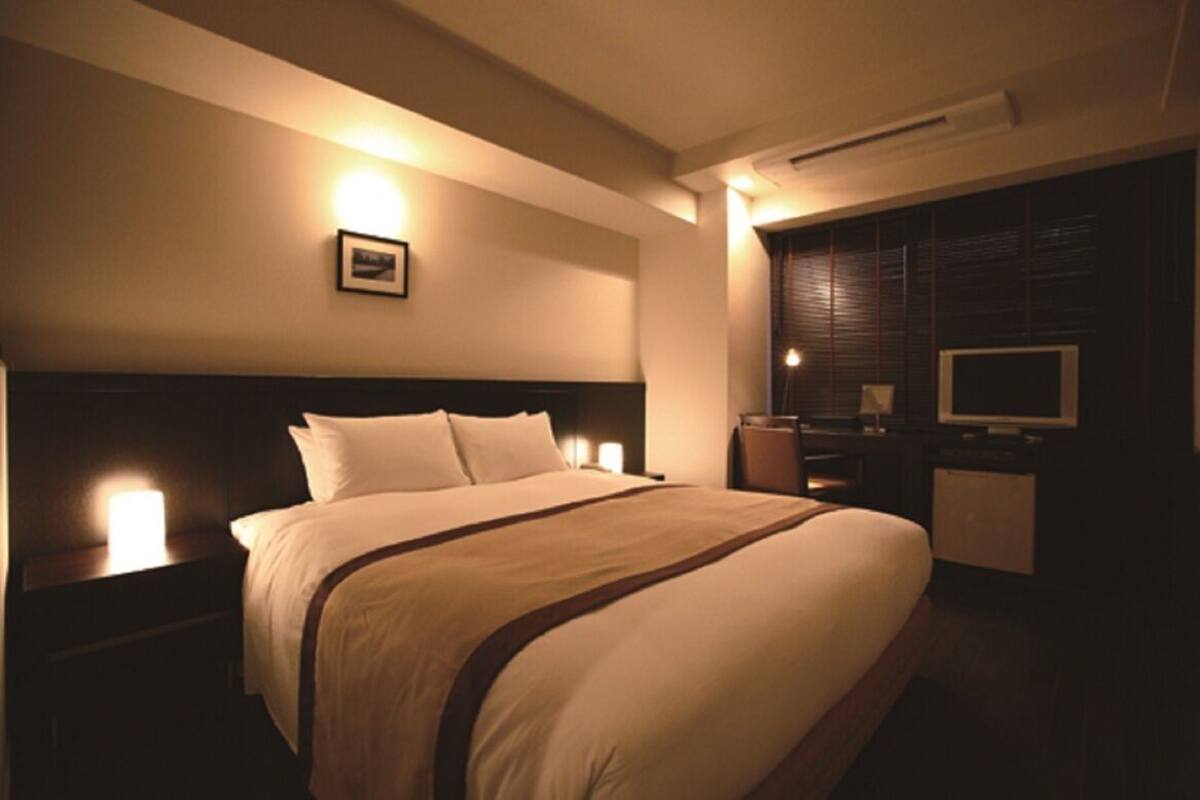 Ein Hotelzimmer mit einem großen Bett, Nachttischlampen, einem Flachbildfernseher und einer Wand-Klimaanlage.