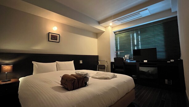 A hotel room with a large bed, a desk with a chair, a television, and a window with blinds. - Sutton Place Hotel Ueno (Tokyo)
