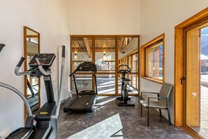 A gym with treadmills, an elliptical, and a chair, with large windows and a view of the outdoors. - Apartment in French Alps with Wellness Centre (Abondance)